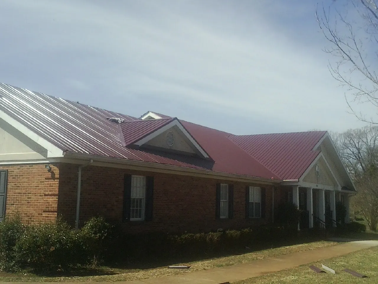 Red metal roof with gabled entries on a long brick building, from a Hail Damage Roof Repair job in Tuscaloosa