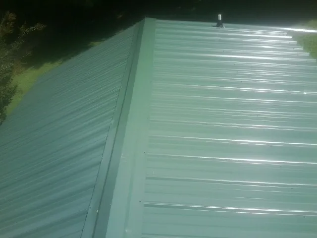 New green metal panels meeting at the ridge of a roof — Flat Roof Repair work by our crew in Tuscaloosa