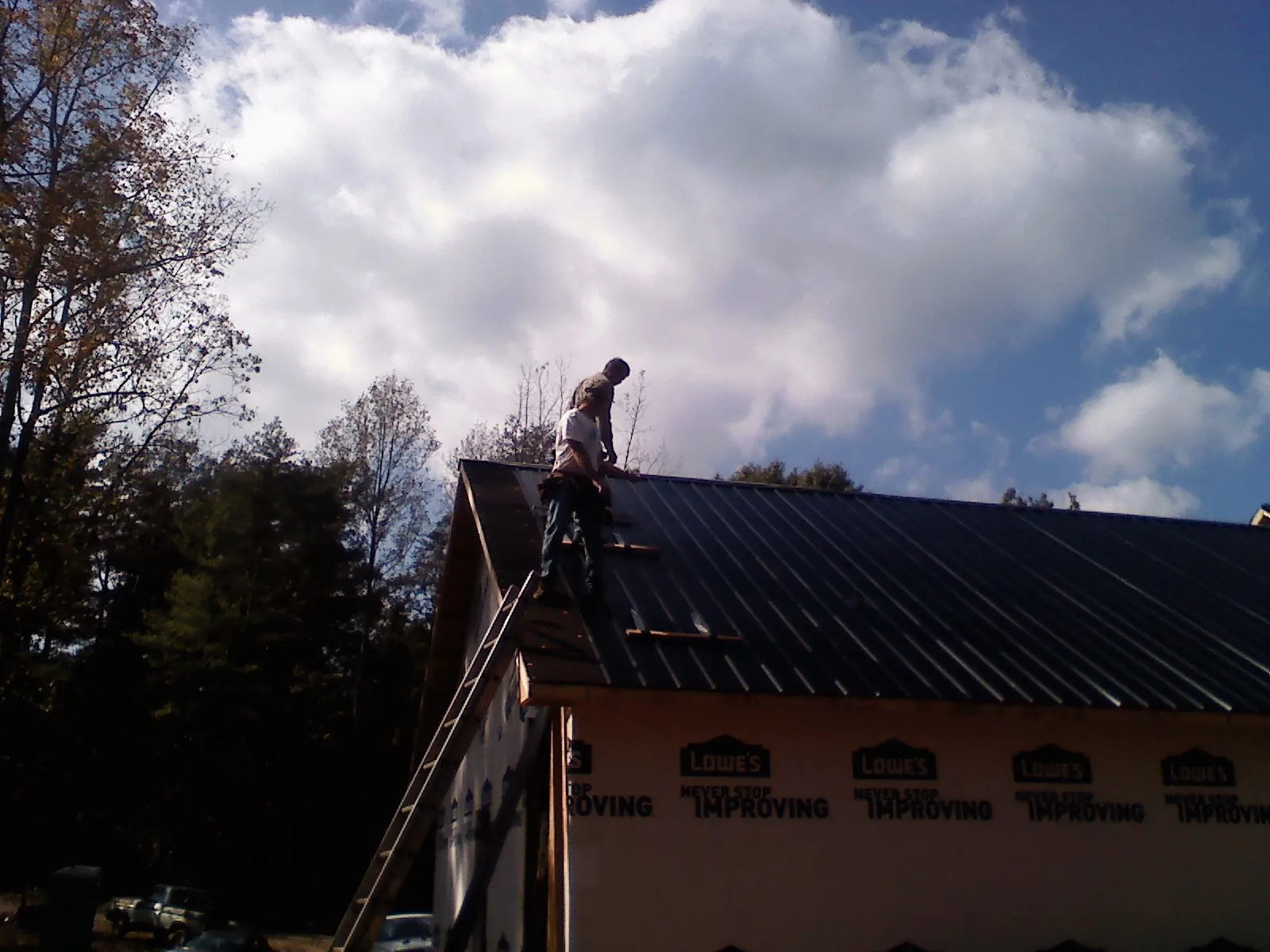 Roofer fastening dark metal panels high against a cloudy sky, from a Roof Inspection job in Tuscaloosa