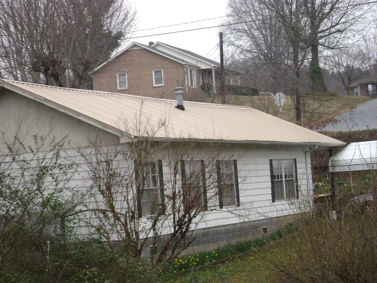 Tan metal roof on a white sided house set into a hillside — Commercial Roofing by Roofing Brothers in Tuscaloosa