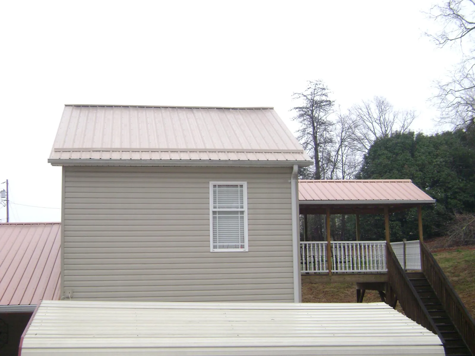 Tan metal roofs on a two story addition and attached porch, from a Roof Replacement job in Tuscaloosa
